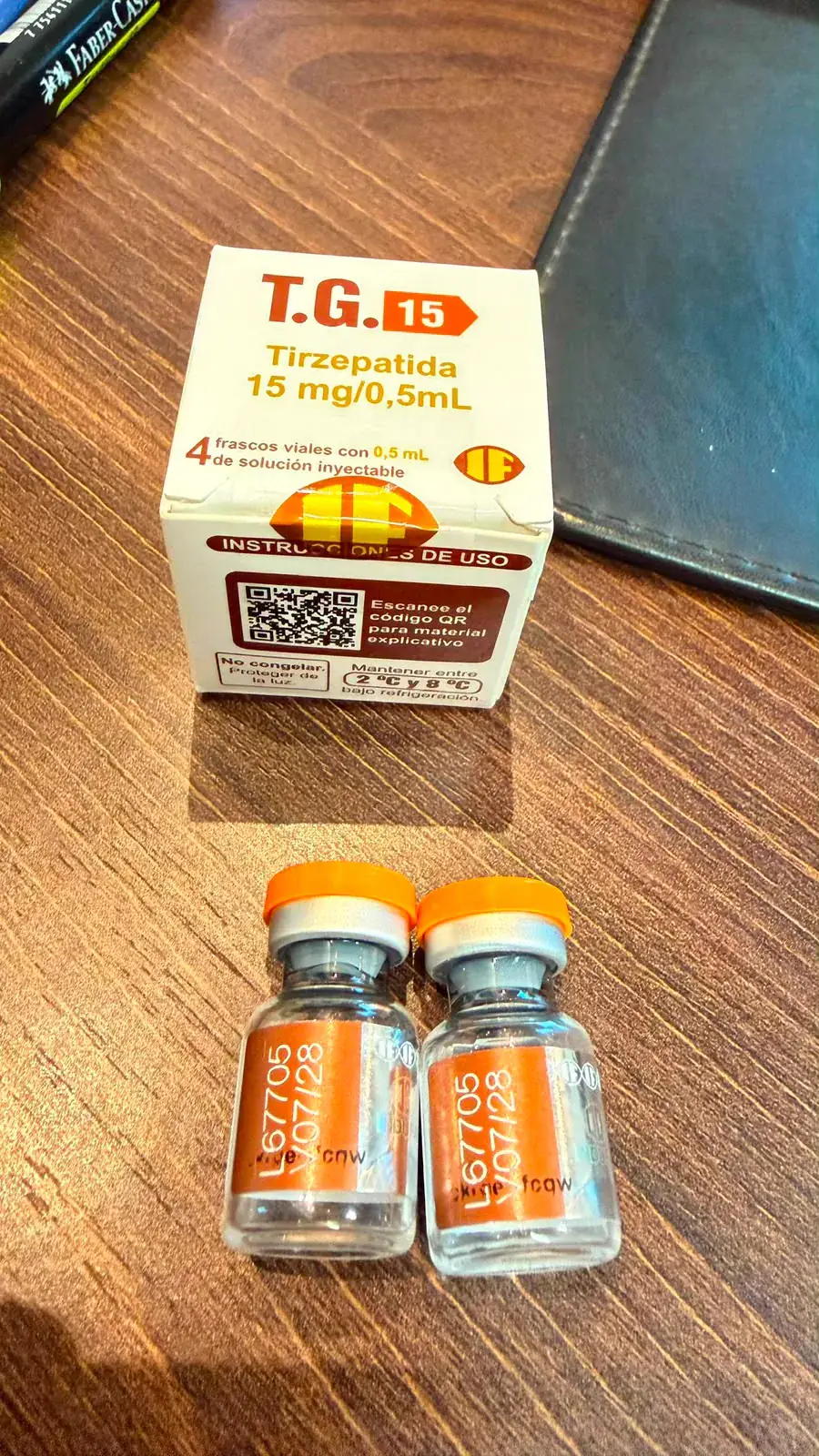 Caixa da TG 15 Tirzepatida 15 mg/0,5 mL ao lado de dois frascos com tampa laranja, lote e validade impressos no rótulo